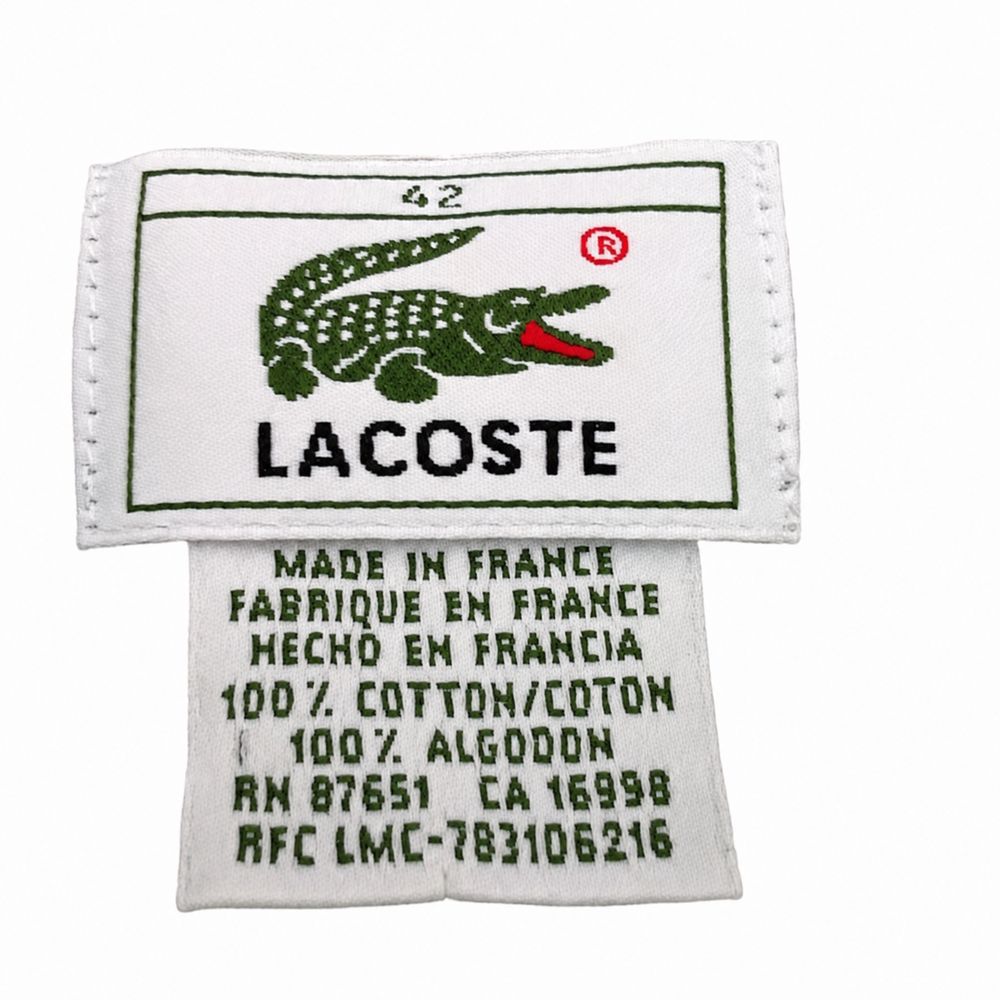緑のLacosteポロに付いたDEVANLAYの多言語ケアタグ