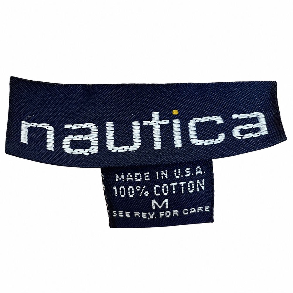 オレンジ色のTシャツに付いたnauticaタグとMade in U.S.A.、100パーセントコットン表示